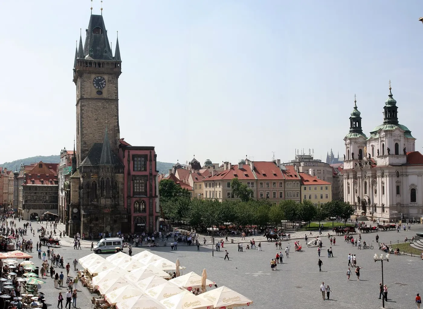 The Old Town Hall tower and the domes of St Nicholas Church across Old Town Square, with café umbrellas in the foreground