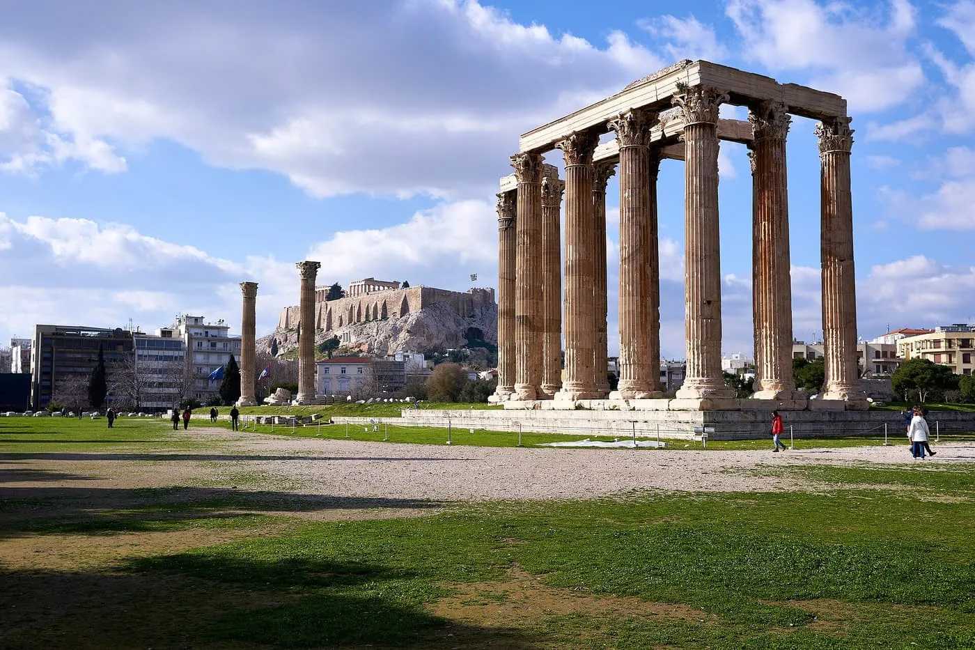 The standing Corinthian columns of the Temple of Olympian Zeus on a grassy plain, with the Acropolis rising behind them