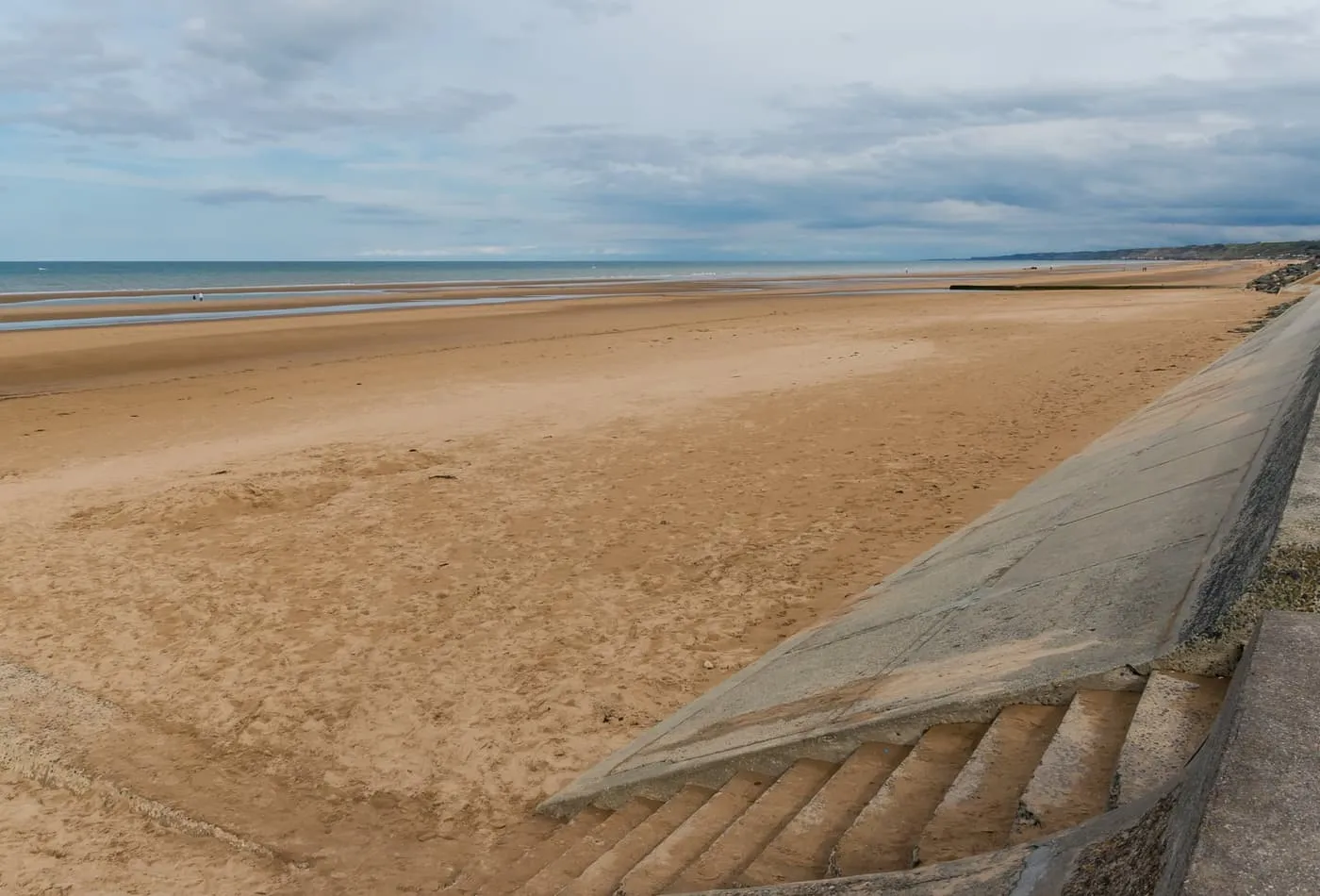 The wide sands of Omaha Beach at low tide beside a concrete sea wall