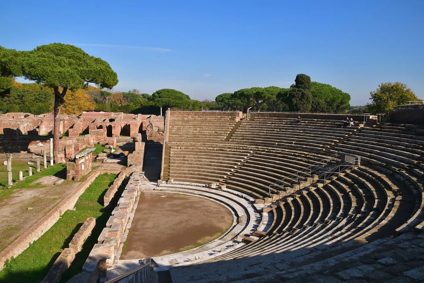 The curved stone seating of the Roman theatre at Ostia Antica, with umbrella pines and ruined brick walls behind