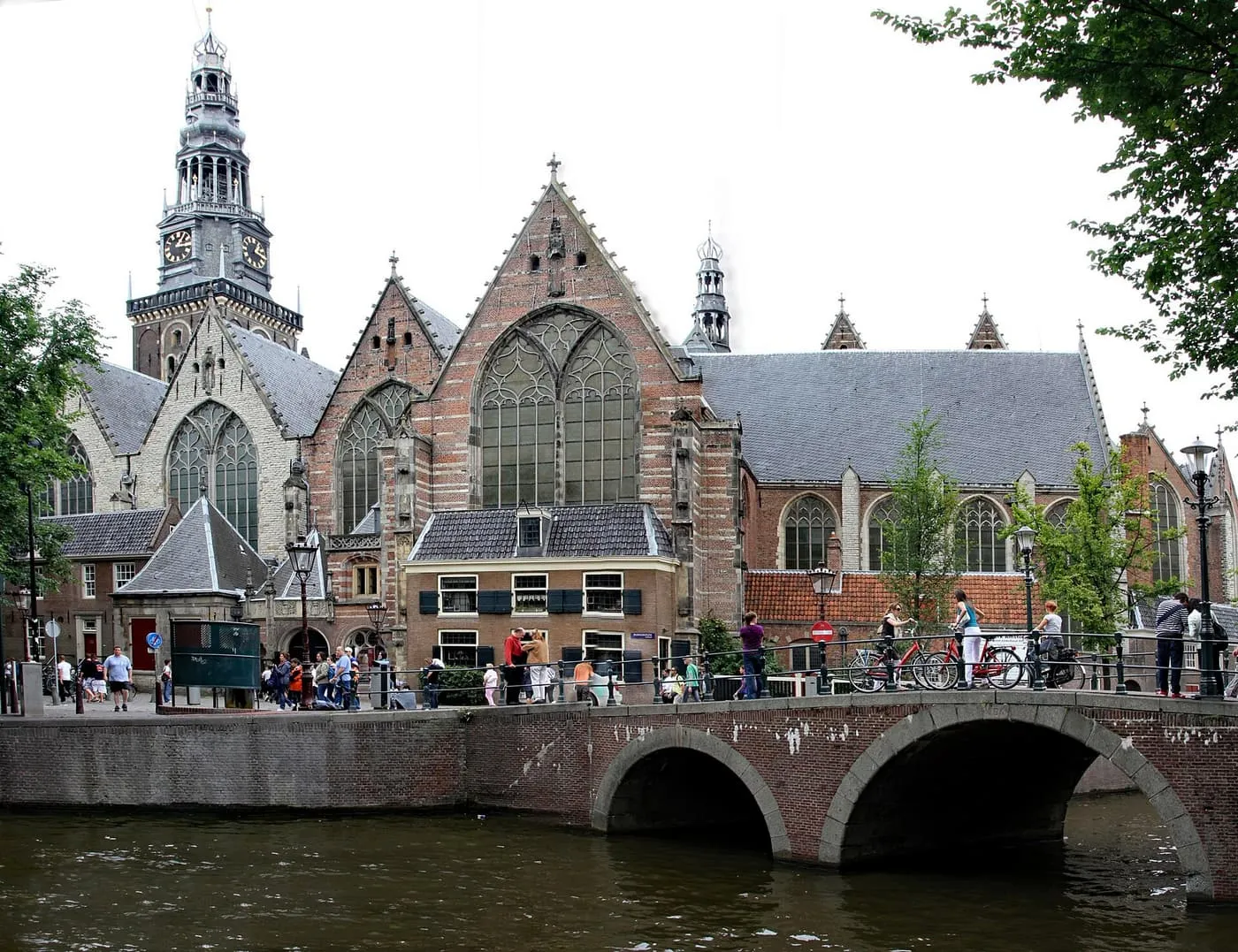 The Oude Kerk's gabled brick front and tall tower beyond a canal bridge, with people and bicycles on the bridge