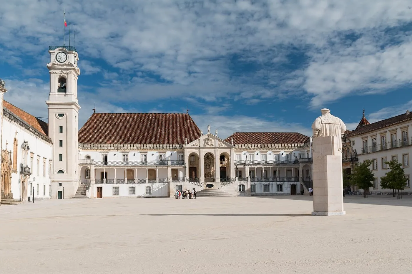 The courtyard of the University of Coimbra, with the clock tower, the Royal Palace and a statue on a plinth