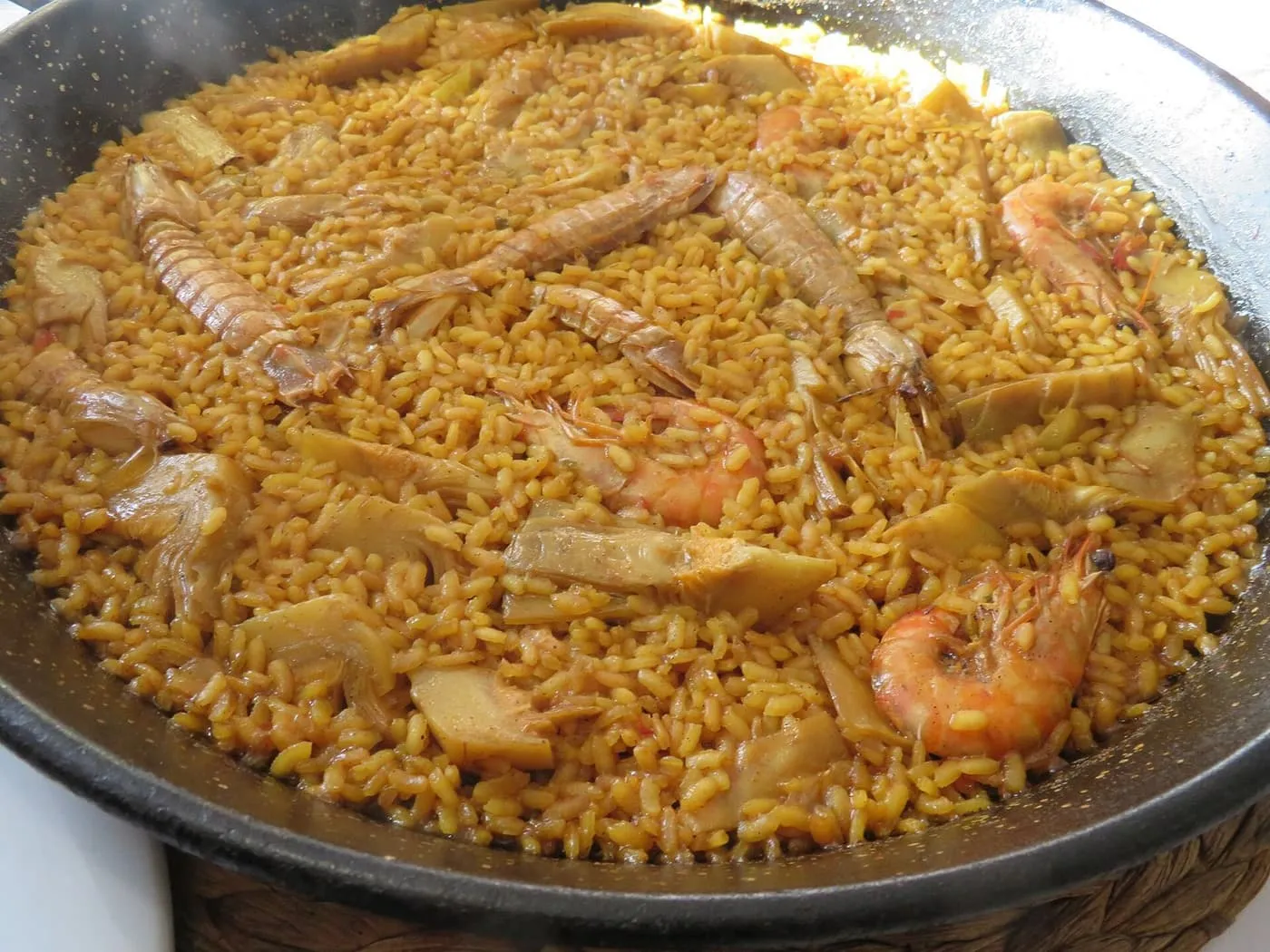 A pan of seafood paella with langoustines and prawns laid over saffron-coloured rice
