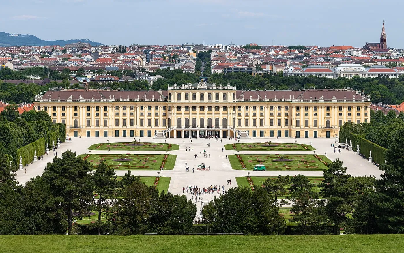 Schönbrunn Palace, a long yellow Baroque façade, seen across the Great Parterre with its four flower beds and the city roofs beyond