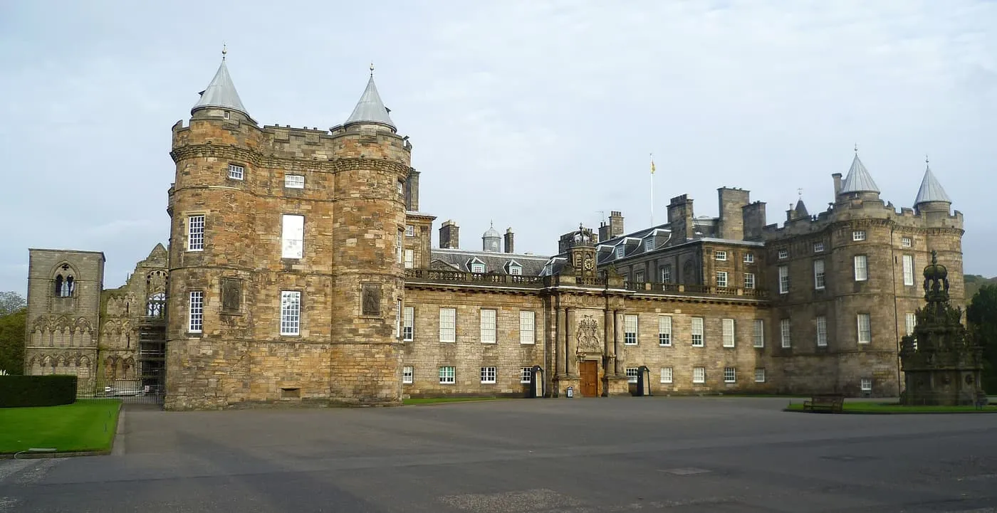 The towers and stone front of the Palace of Holyroodhouse, with the ruined abbey at the left and a stone fountain at the right
