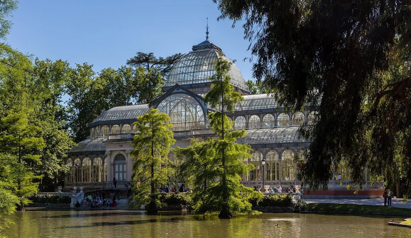 The glass dome and iron-framed walls of the Palacio de Cristal, seen across the pond with trees in front