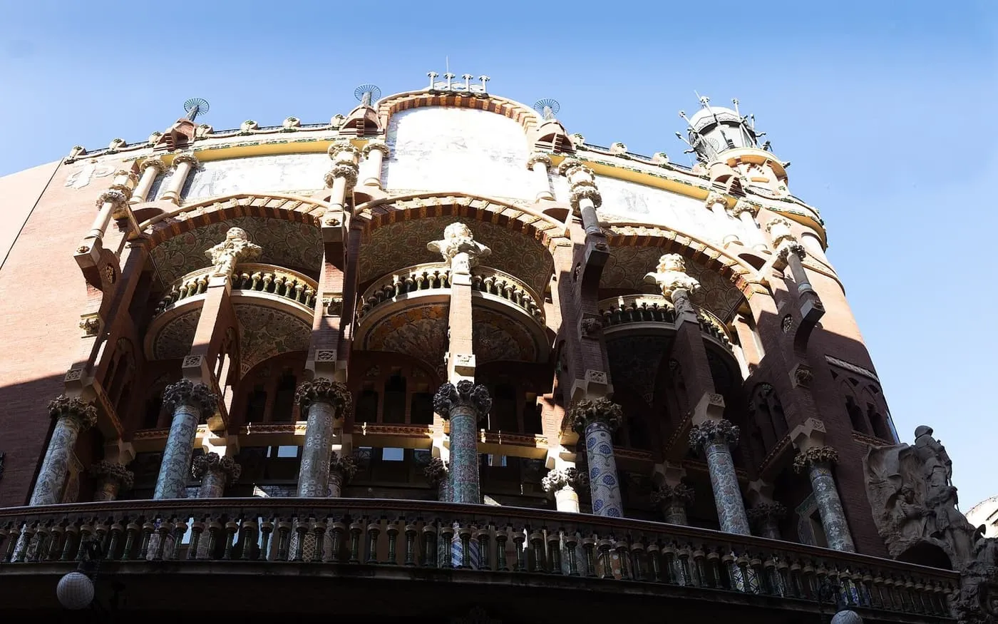 The upper façade of the Palau de la Música Catalana, with tiled columns, balconies and a mosaic frieze against a blue sky