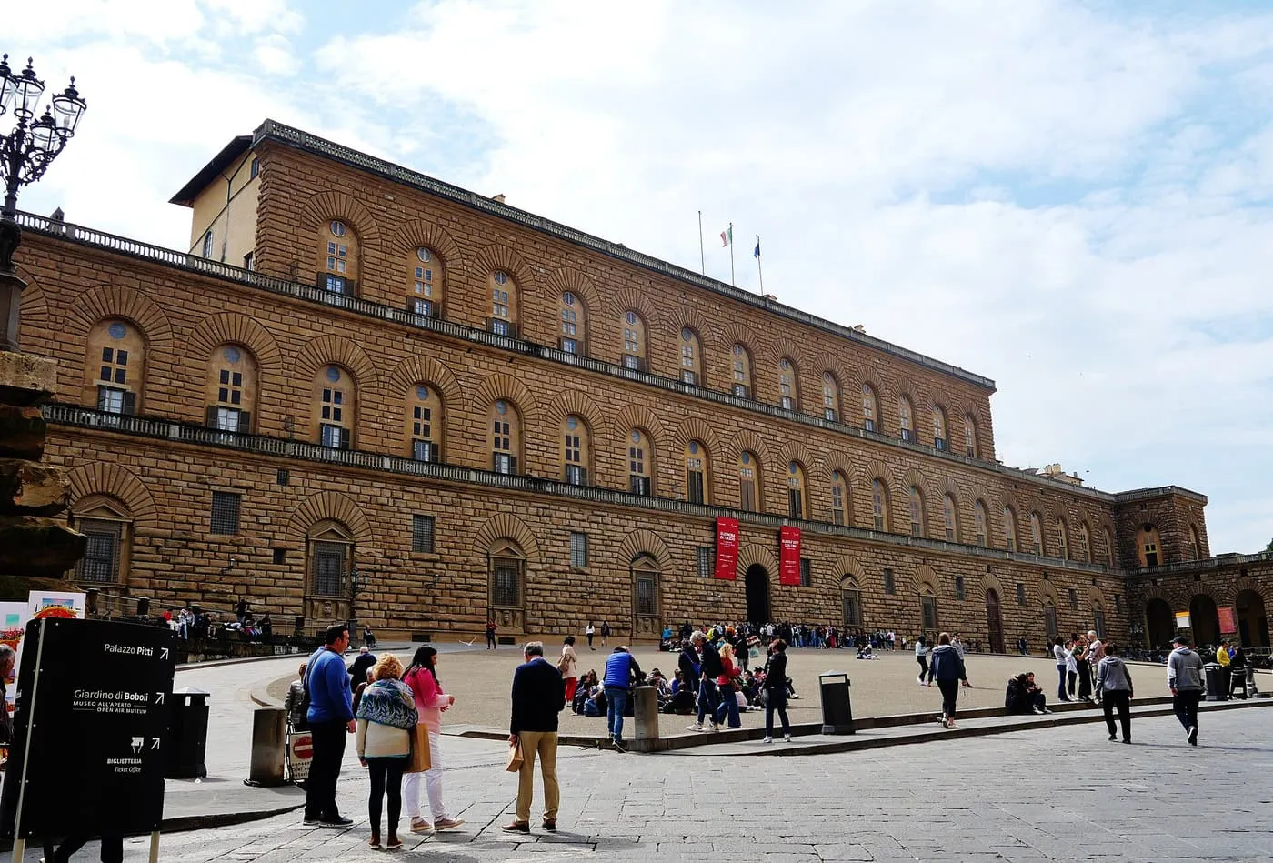 The long rusticated stone front of the Pitti Palace across its sloping piazza, with visitors in front