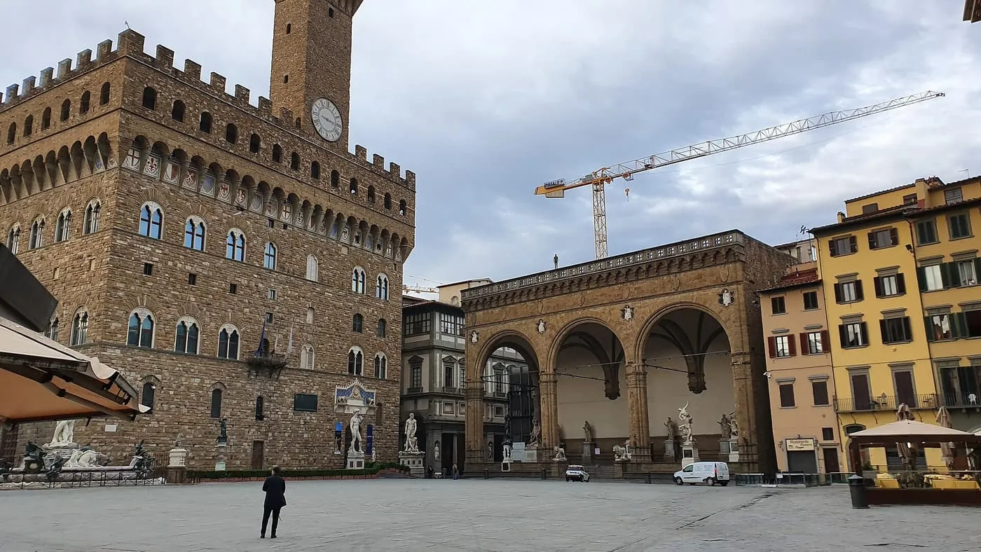 Palazzo Vecchio with its crenellated top and clock tower beside the Loggia dei Lanzi, across Piazza della Signoria