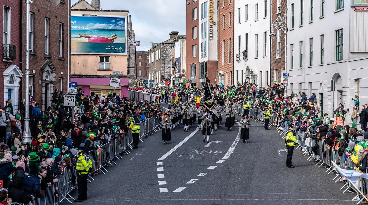 A marching band coming down a Dublin street between crowds behind metal barriers during the St Patrick's Day parade