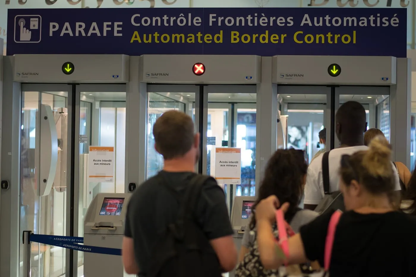 Travellers queuing at the PARAFE automated border control gates at a Paris airport, under a sign reading Contrôle Frontières Automatisé
