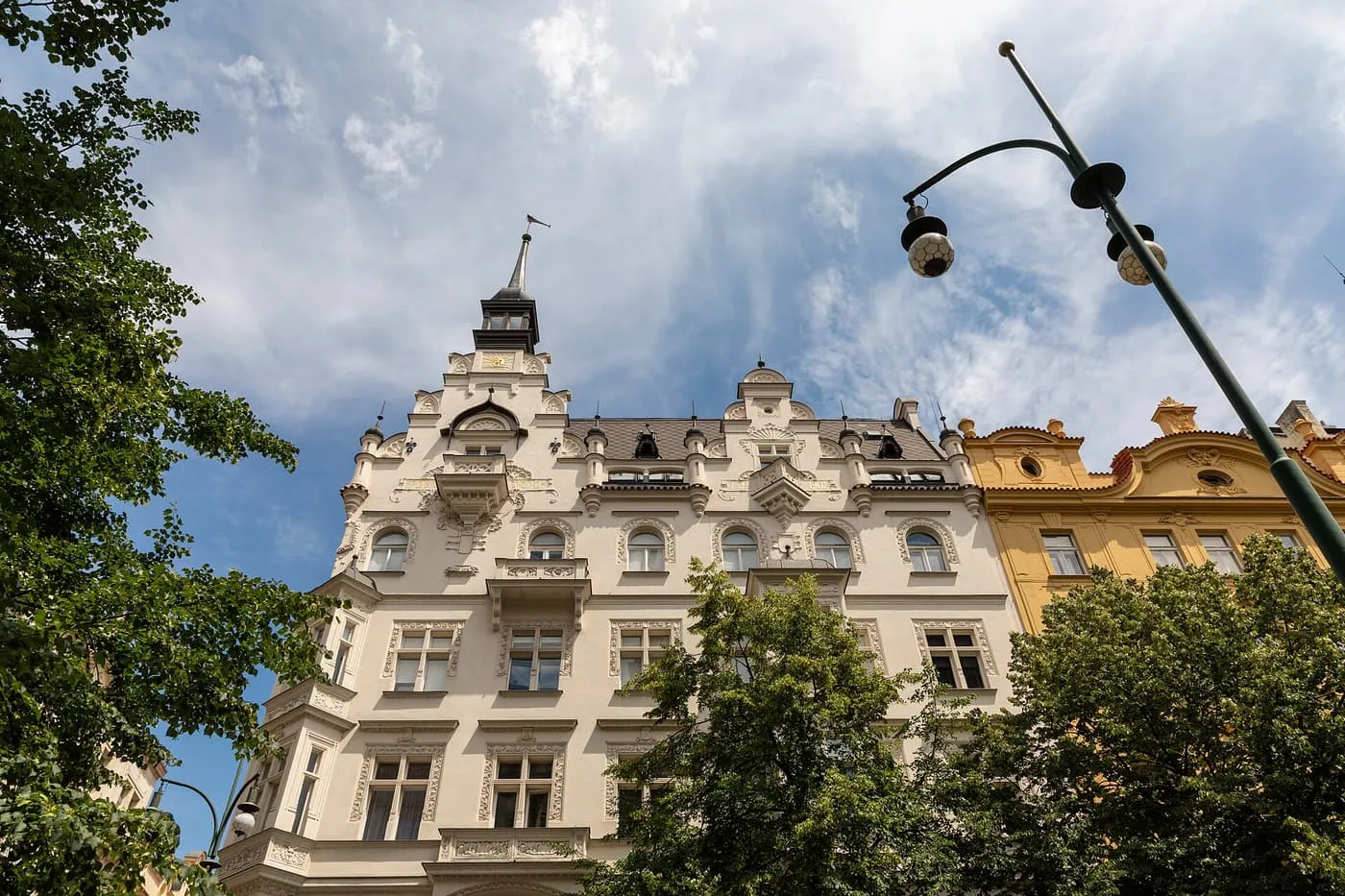 The Art Nouveau facade of a house on Pařížská street in Josefov, with tall windows and a corner turret, seen from below between trees