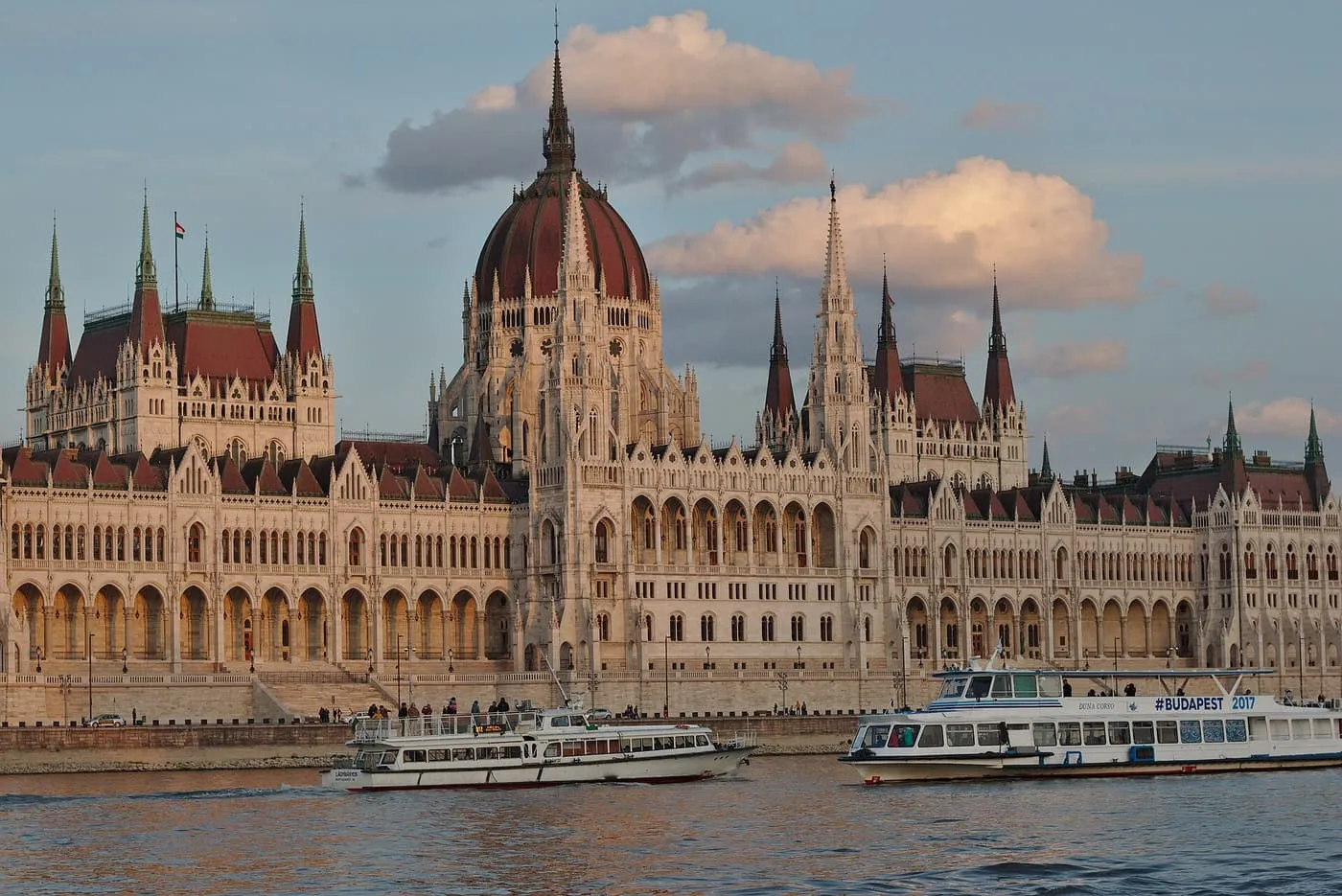 The Hungarian Parliament on the Pest bank in evening light, with two sightseeing boats on the Danube