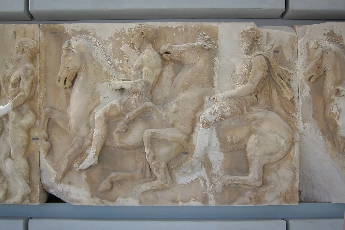Horsemen and horses carved in relief on a block of the Parthenon frieze, set in a grey frame