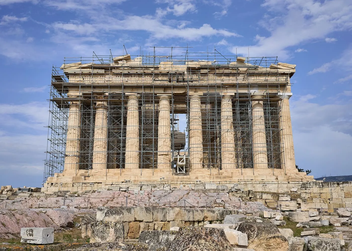 The west front of the Parthenon, its Doric columns standing behind scaffolding, above the rock and fallen blocks of the Acropolis