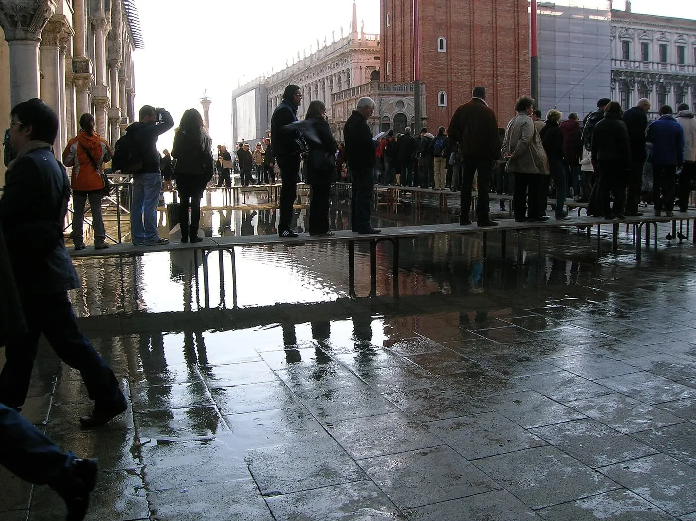 Visitors standing in a line on a raised wooden walkway above the flooded Square
