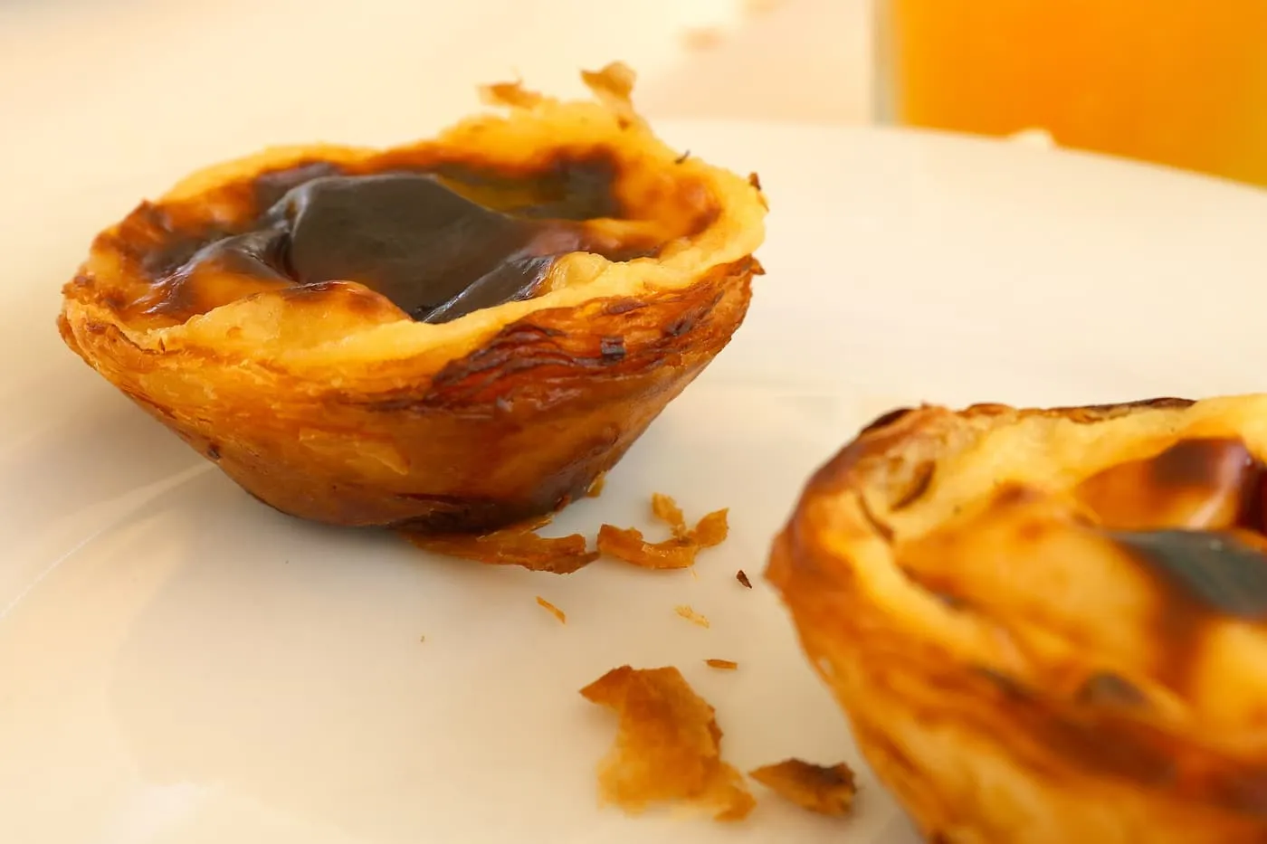 Two pastéis de Belém on a white plate, with the flaky pastry shells and scorched custard tops