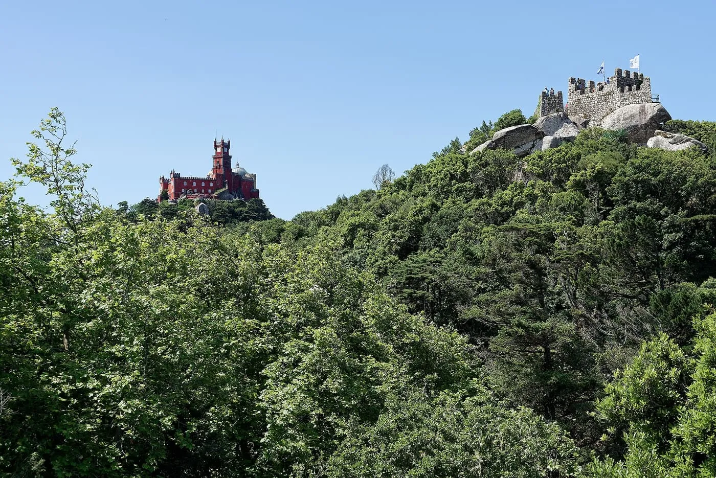 Pena Palace's red tower on one forested hilltop and the Moorish Castle's walls on another, under a clear sky