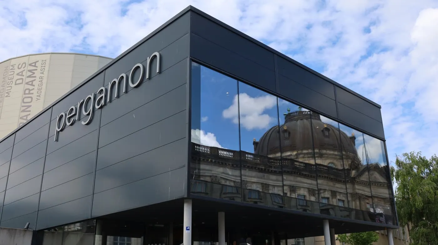 The dark glass-fronted Pergamon Panorama building with the Panorama drum behind it and the Bode-Museum dome reflected in the glass