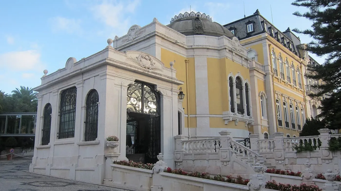 The yellow and cream façade of Pestana Palace, a 19th-century palace with a domed pavilion and balustraded steps