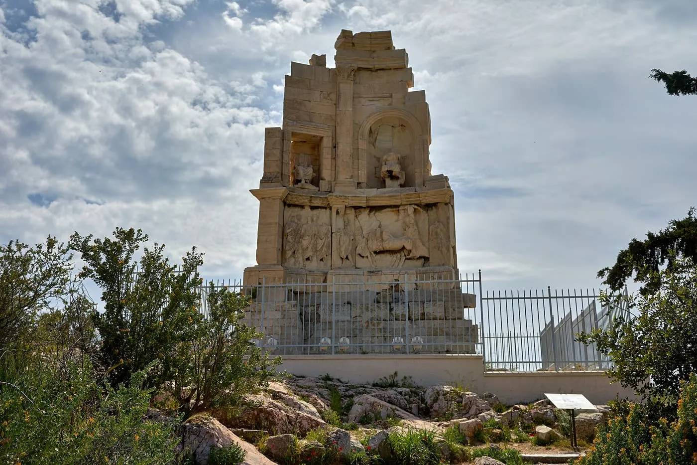 The weathered marble Philopappos Monument on its hilltop behind an iron fence, with relief carvings and two statues in niches