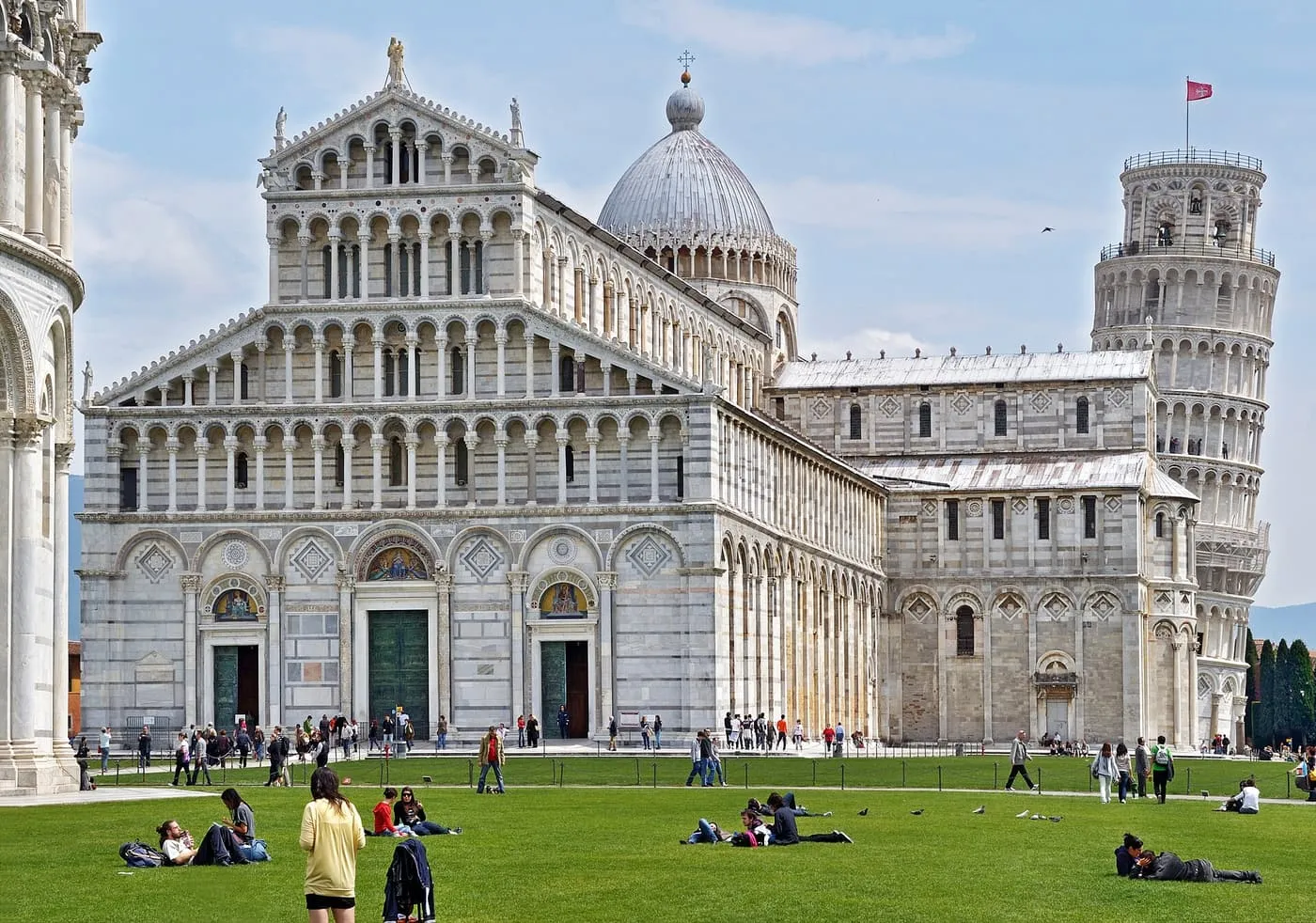 The marble front of Pisa Cathedral with the Leaning Tower beyond, seen across the lawn of the Piazza dei Miracoli