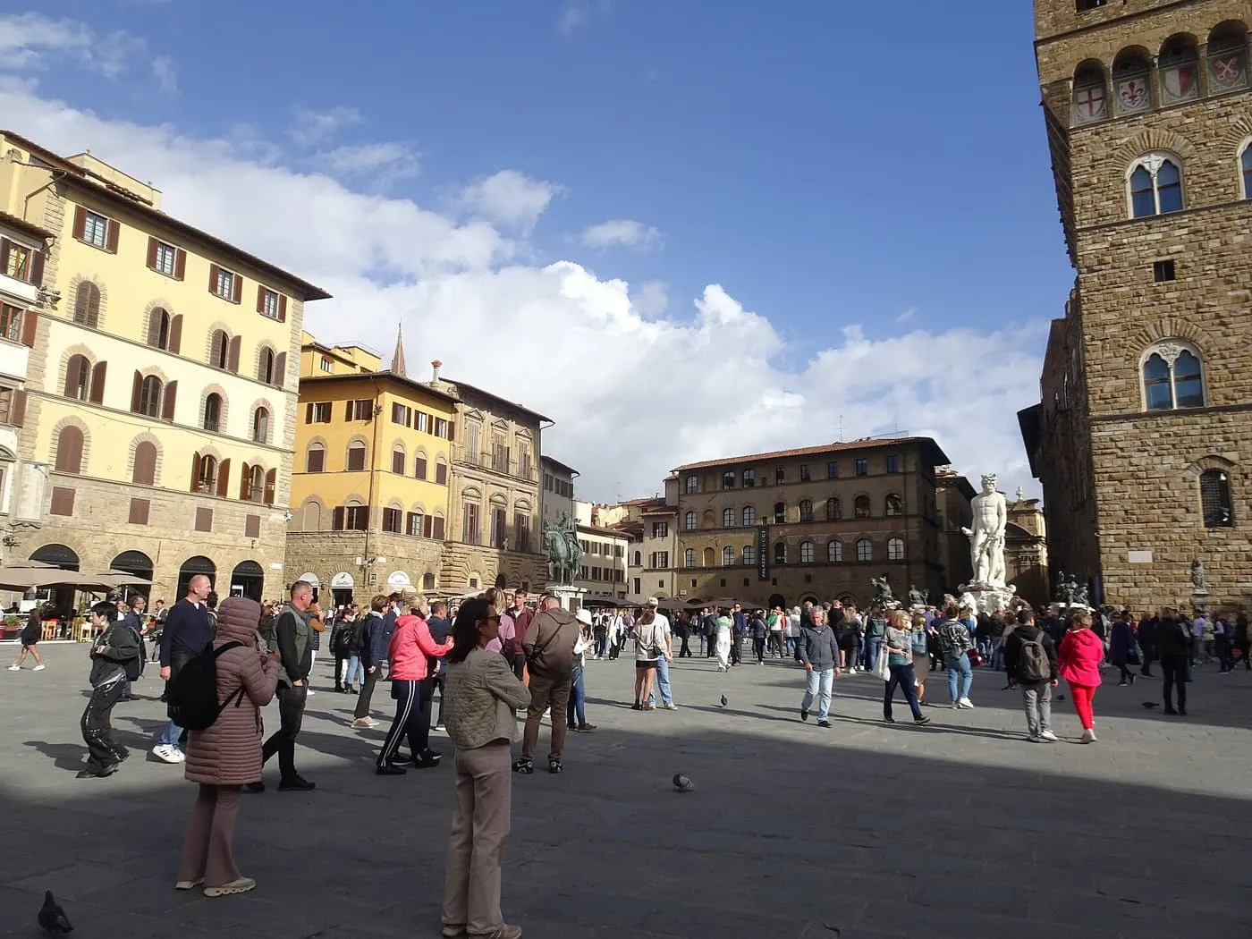 Visitors crossing the open Piazza della Signoria, with the Neptune Fountain in the background and the side of Palazzo Vecchio at right