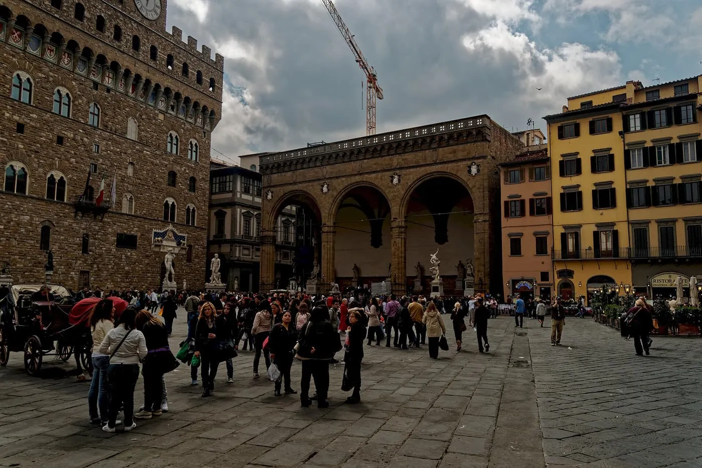 The tower of Palazzo Vecchio and the arches of the Loggia dei Lanzi on Piazza della Signoria, with crowds crossing the paving