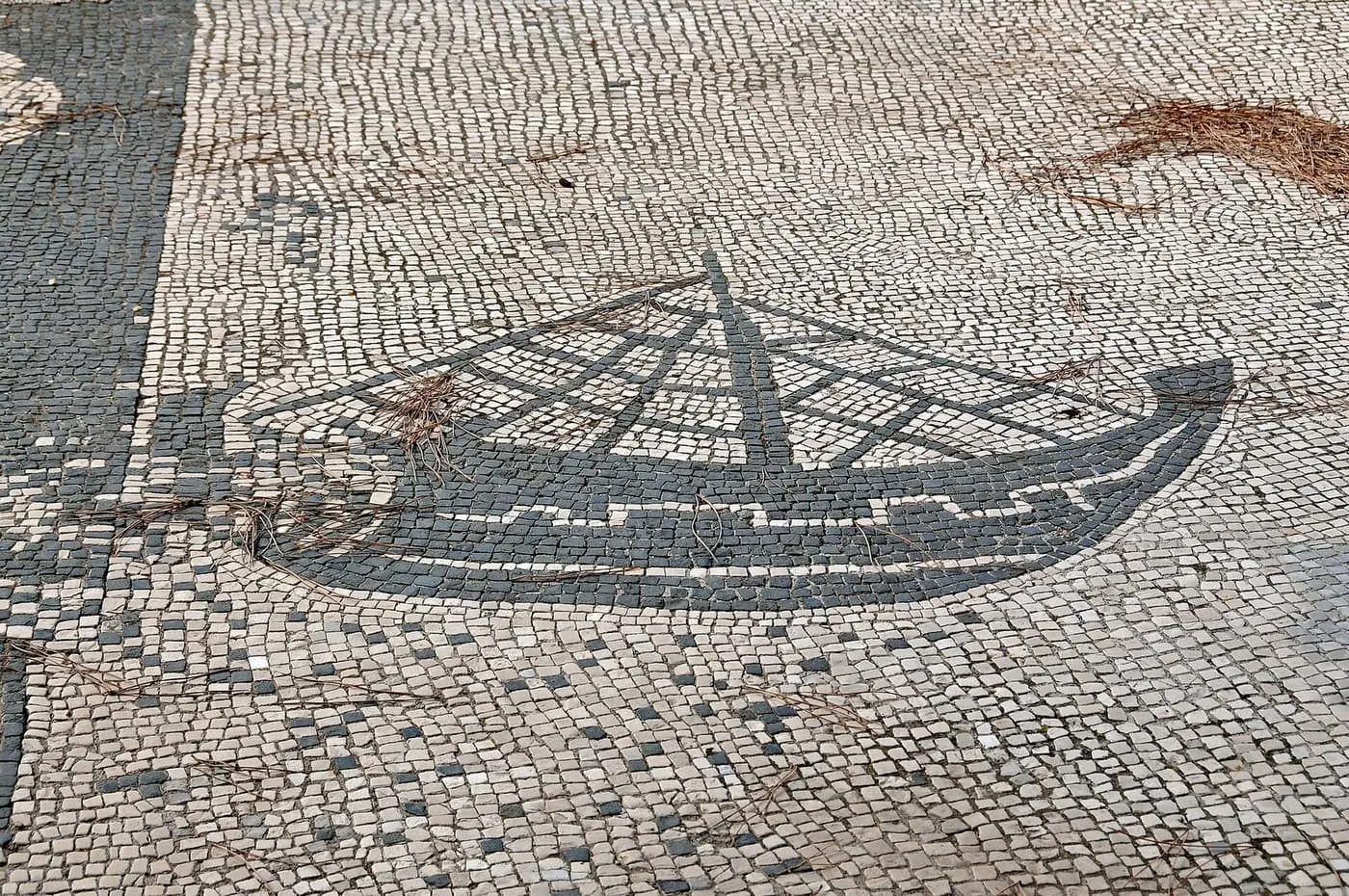 A black-and-white floor mosaic of a ship with its rigging, in the Piazzale delle Corporazioni