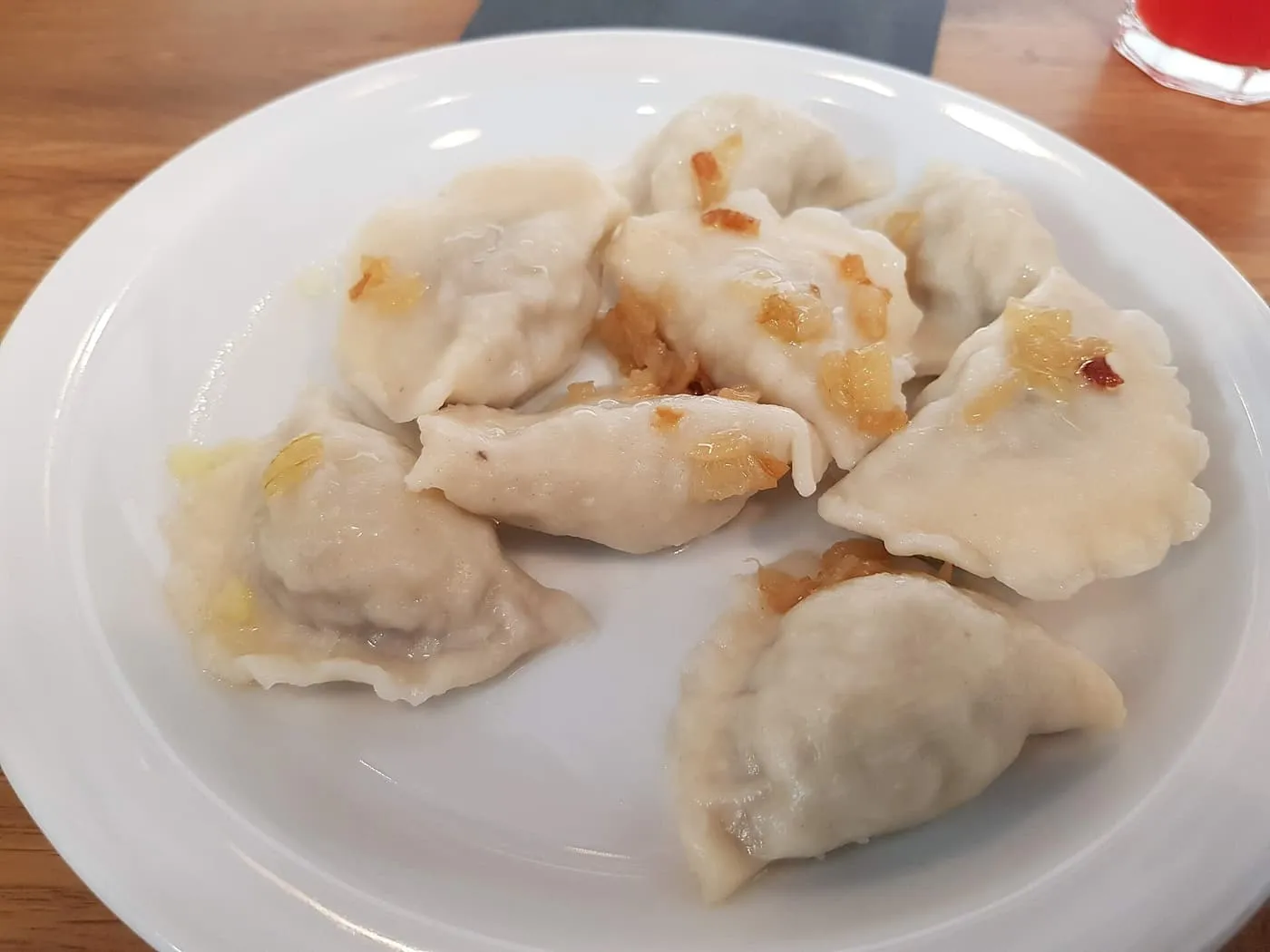A white plate of boiled pierogi topped with fried onion