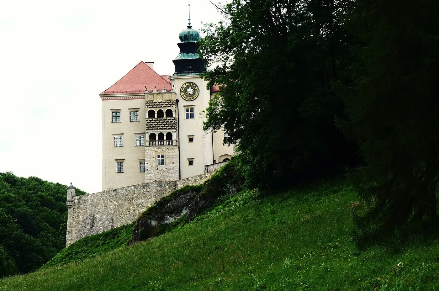 The white walls and clock tower of Pieskowa Skała castle above a grassy slope