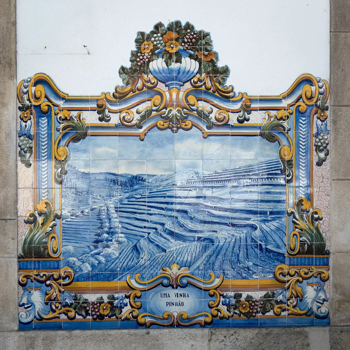 A blue and white tile panel of terraced vineyards in a gilded frame, labelled Uma Vinha, Pinhão, on the wall of Pinhão railway station
