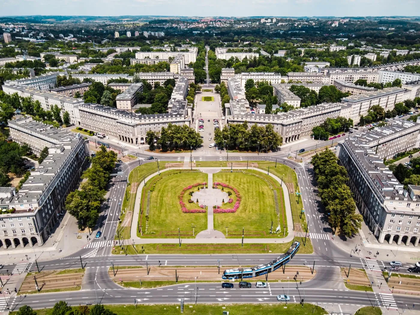 Plac Centralny in Nowa Huta from the air, a lawn with flower beds between long apartment blocks, with a tram crossing at the bottom