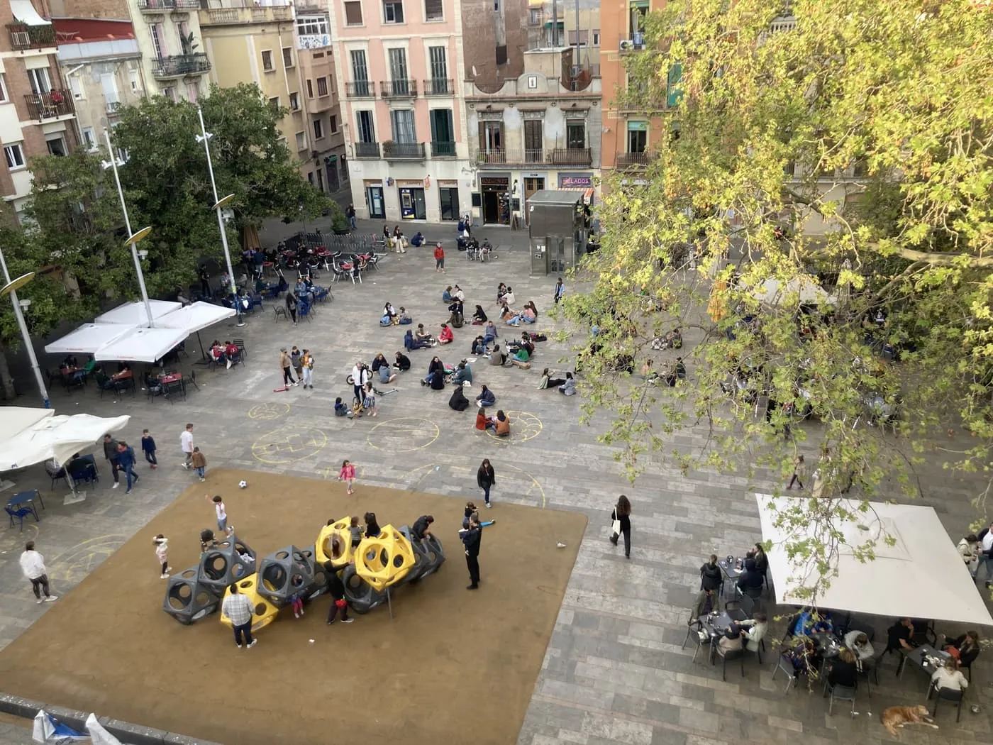 An aerial view of Plaça del Sol, a sunken square with a play area at its foot, café terraces under awnings and old buildings round the sides
