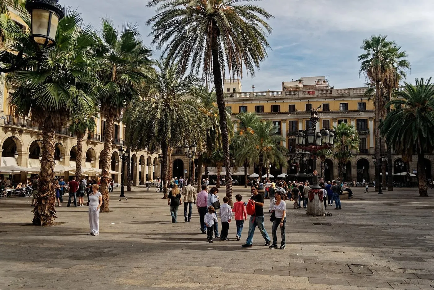 Plaça Reial: a paved square with palm trees, arcaded yellow buildings and a group of visitors crossing it