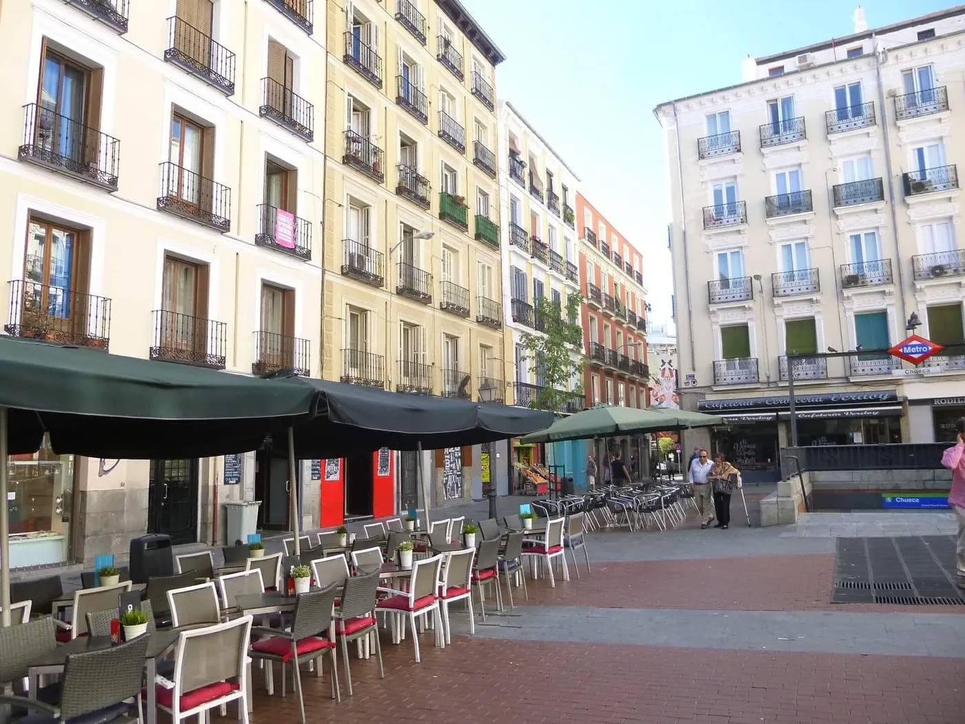 Café terraces and cream apartment blocks with iron balconies on the Plaza de Chueca, with the Metro Chueca sign on the right