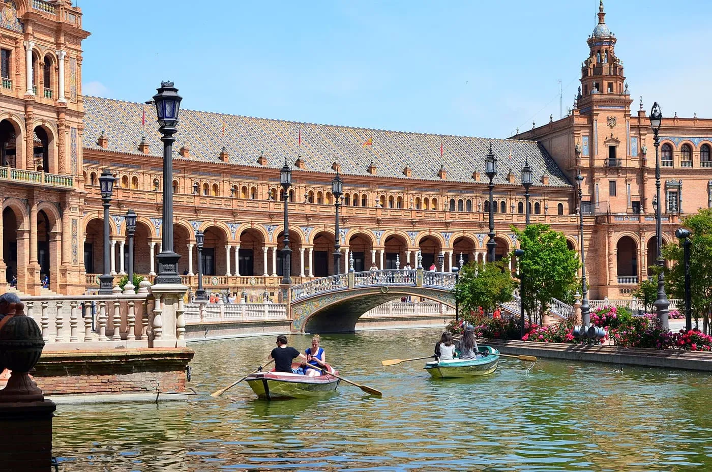 Rowing boats on the canal in the Plaza de España, with its arcaded brick building and a tower behind