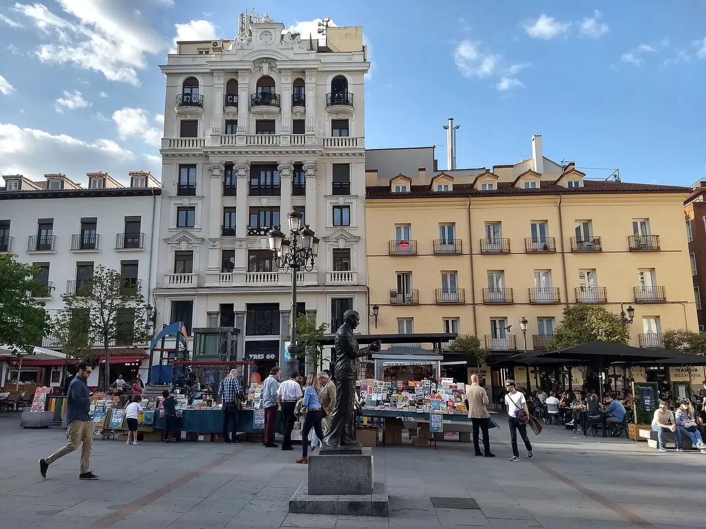 The Plaza de Santa Ana by day, with a statue, book stalls and café terraces in front of cream and ochre buildings