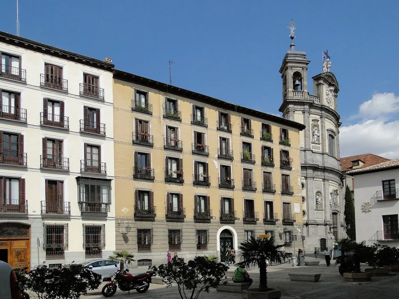 Apartment blocks with wrought-iron balconies on the Plaza del Cordón in Madrid, with the bell tower of St Michael's Basilica at right