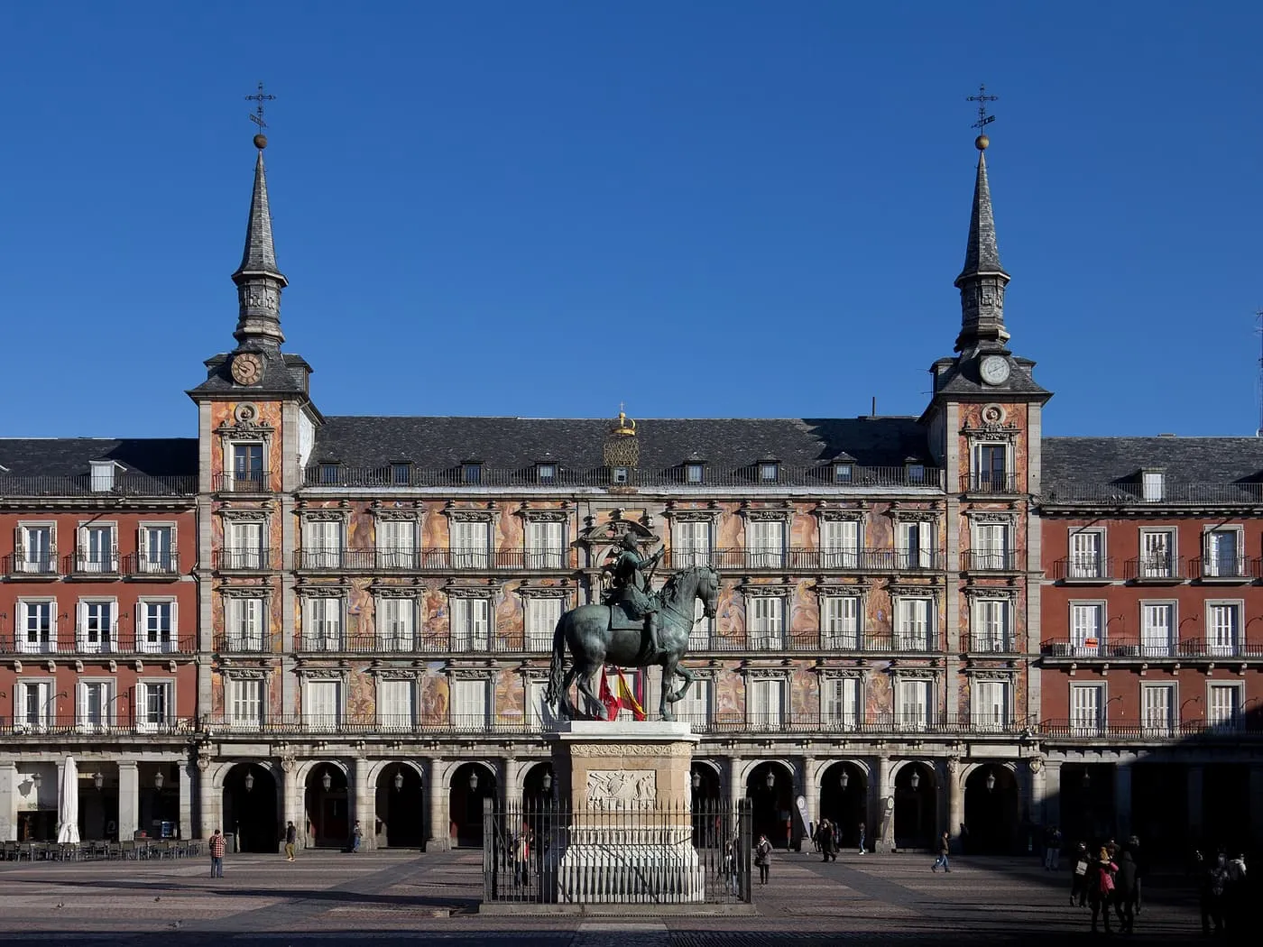The equestrian statue of Philip III in the Plaza Mayor, in front of the Casa de la Panadería with its painted façade, two slate spires and arcade below