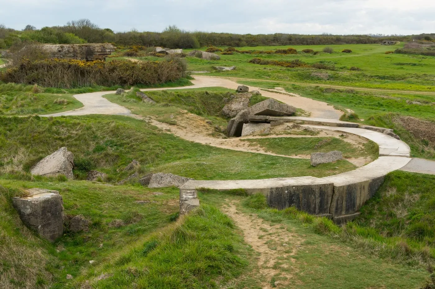 Paths winding between bomb craters and broken German gun emplacements on the grass at Pointe du Hoc