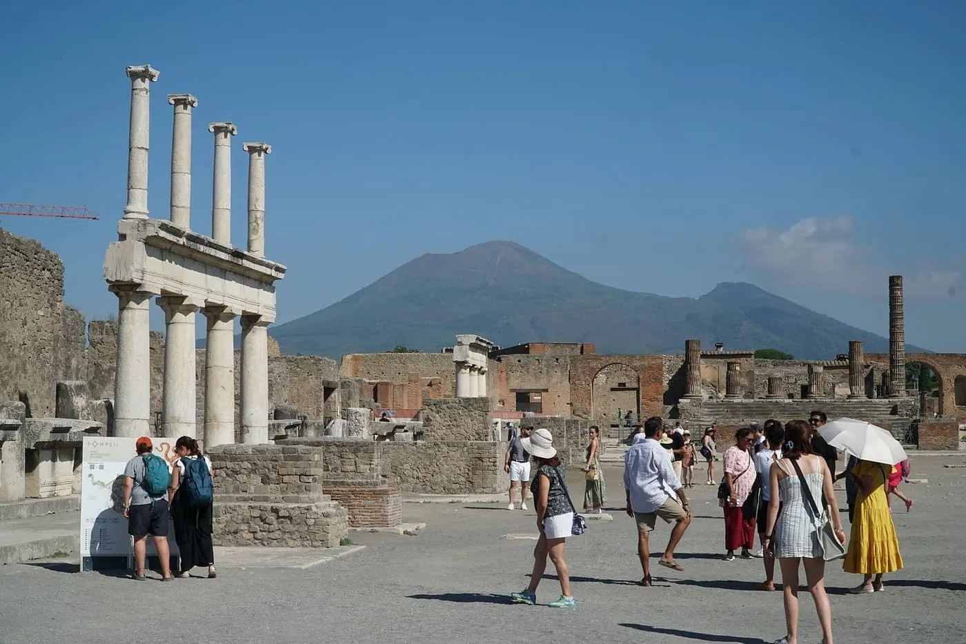 Columns in the Forum at Pompeii, with visitors in the open square and Vesuvius behind