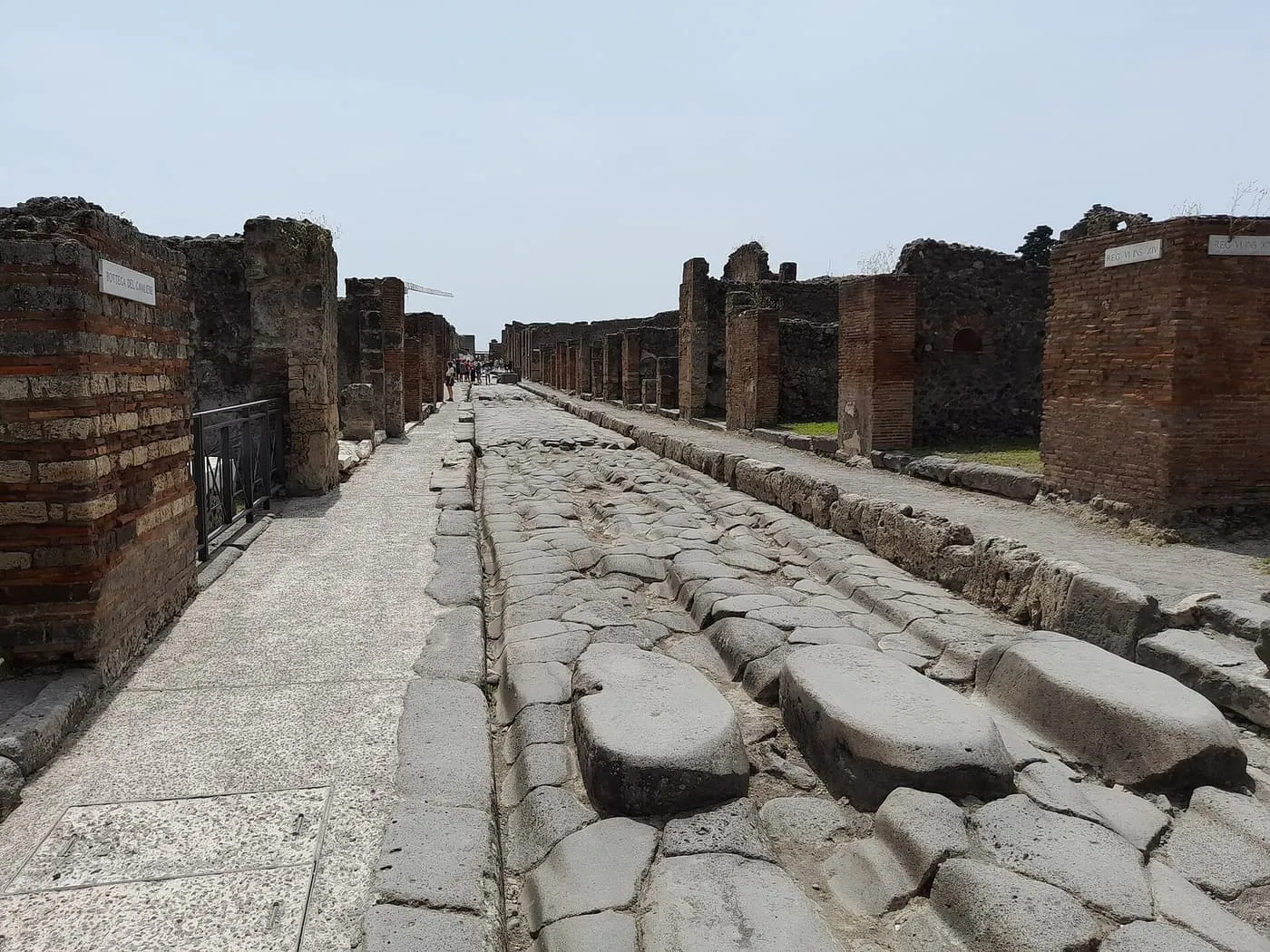 A paved street in Pompeii with raised stepping stones across the road and ruined shopfronts on either side