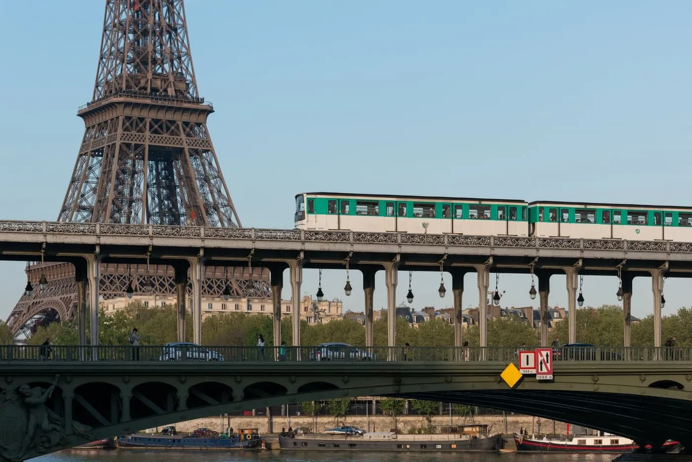 A green-and-white metro train crossing the Pont de Bir-Hakeim on its iron viaduct, with the Eiffel Tower rising behind it in daylight