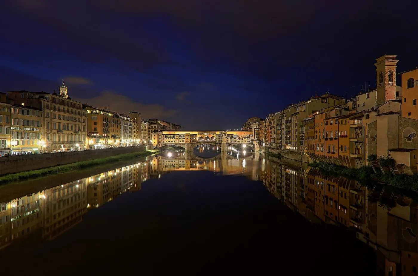 The Ponte Vecchio lit at dusk, its shops glowing yellow above their reflection in the Arno