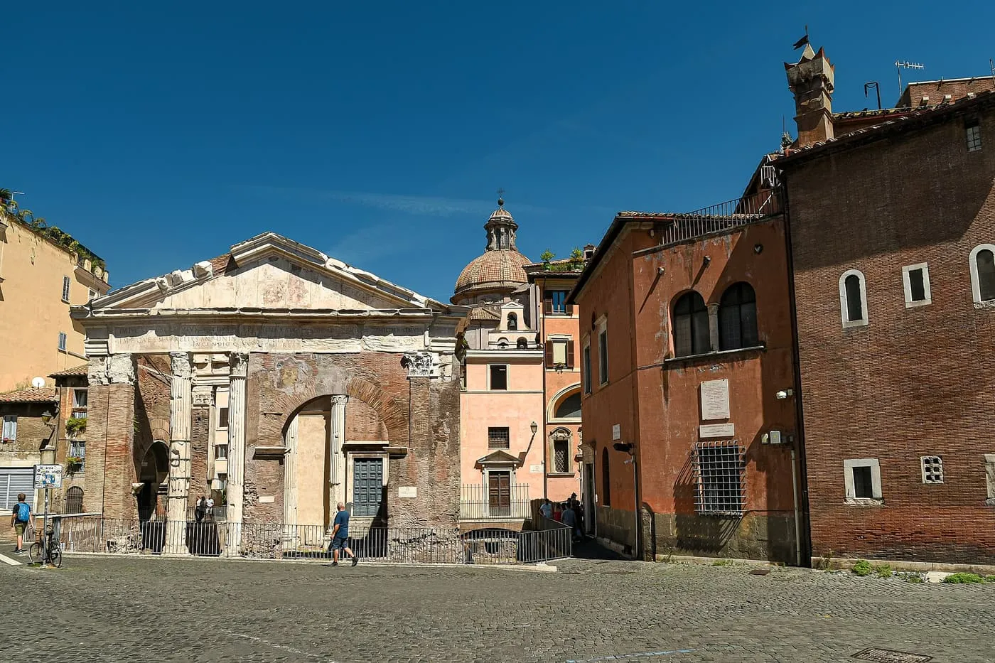 The brick and marble ruin of the Portico d'Ottavia, with its pediment and columns, beside the church built into it, in a cobbled square