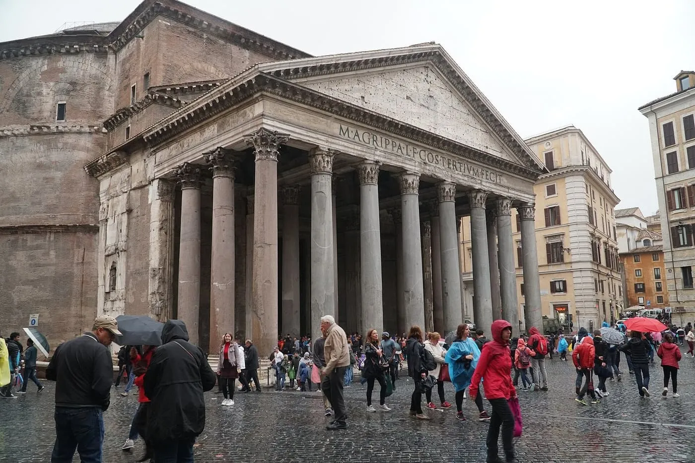 The Pantheon's portico of granite columns in Piazza della Rotonda, with the inscription of Agrippa across the front and visitors in rain gear in the square
