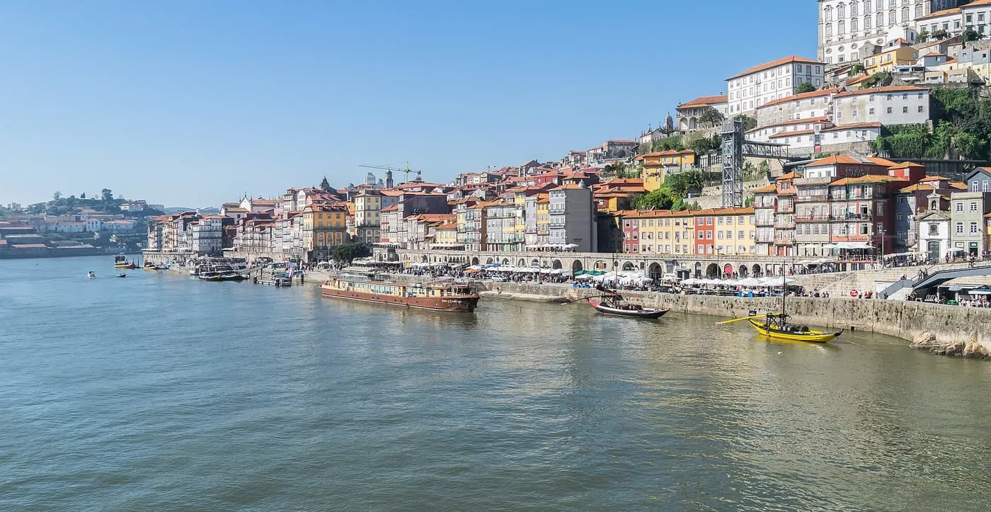 Colourful houses of Porto's Ribeira rising from the Douro quayside, with a moored boat and a yellow rabelo boat