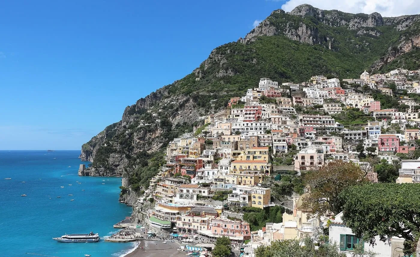 Pastel houses stacked up a steep hillside above the sea at Positano, with a ferry at the beach
