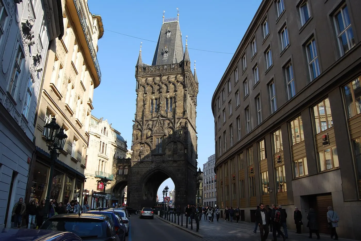 The dark Gothic Powder Gate Tower rising above the street, seen through the gap between buildings